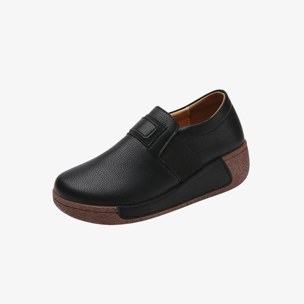 Mocassini con zeppa da donna in pelle sintetica nera, dal design ergonomico per un comfort ottimale. Queste scarpe hanno una suola marrone spessa e texturizzata, che offre un eccellente sostegno. Il loro stile pulito con chiusura elastica facilita la calzata restando elegante e pratico.