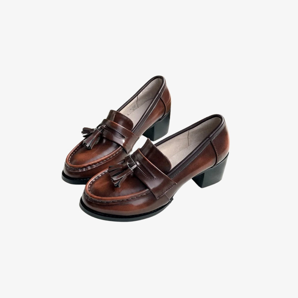 Mocassini da donna in pelle marrone, ornati sul collo del piede da nappe decorative per uno stile classico ed elegante. Queste scarpe hanno tacchi quadrati neri, che offrono comfort e stabilità, ideali per un'allure sofisticata di ogni giorno.