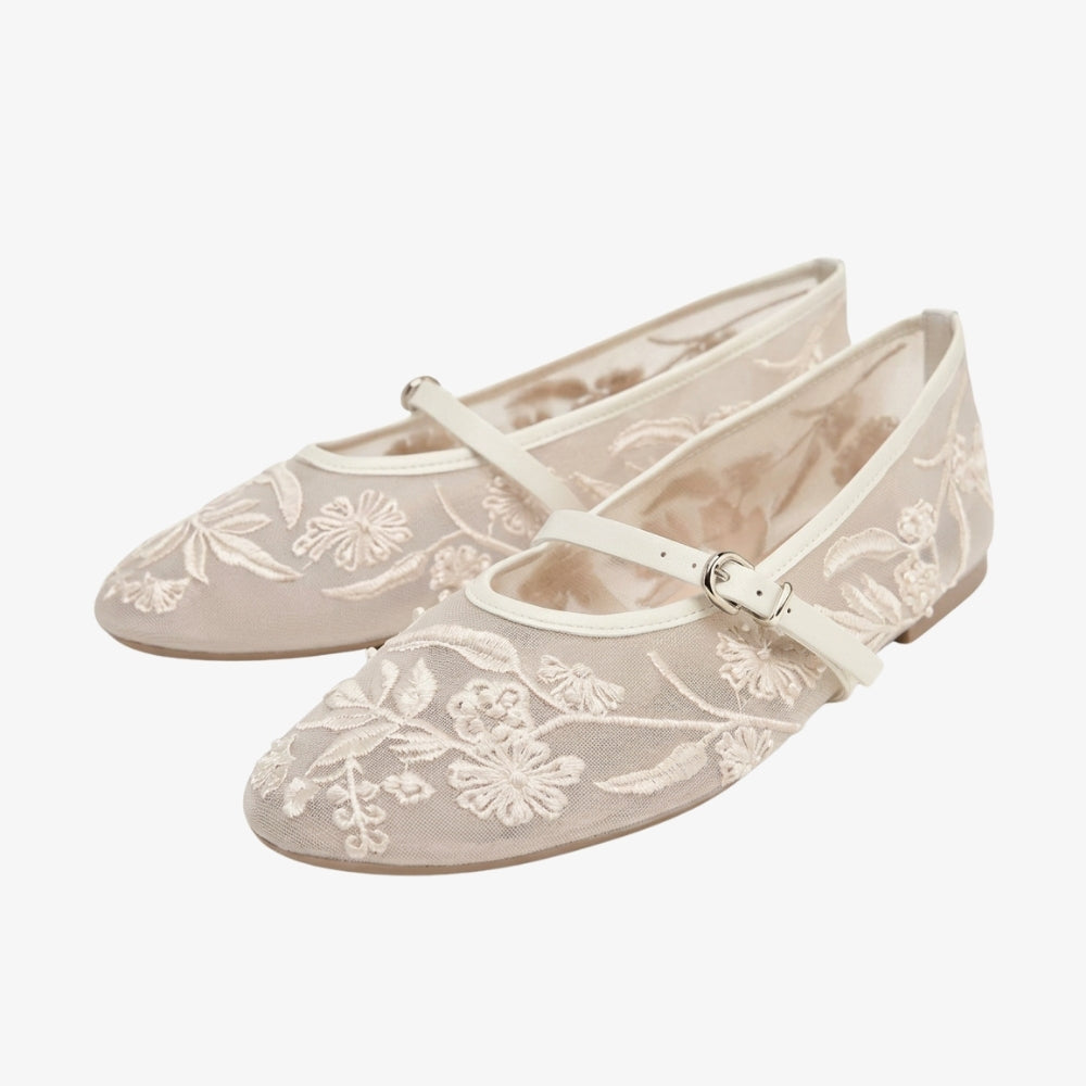 Mocassino ballerina di colore bianco con ricami floreali e un cinturino, su sfondo grigio