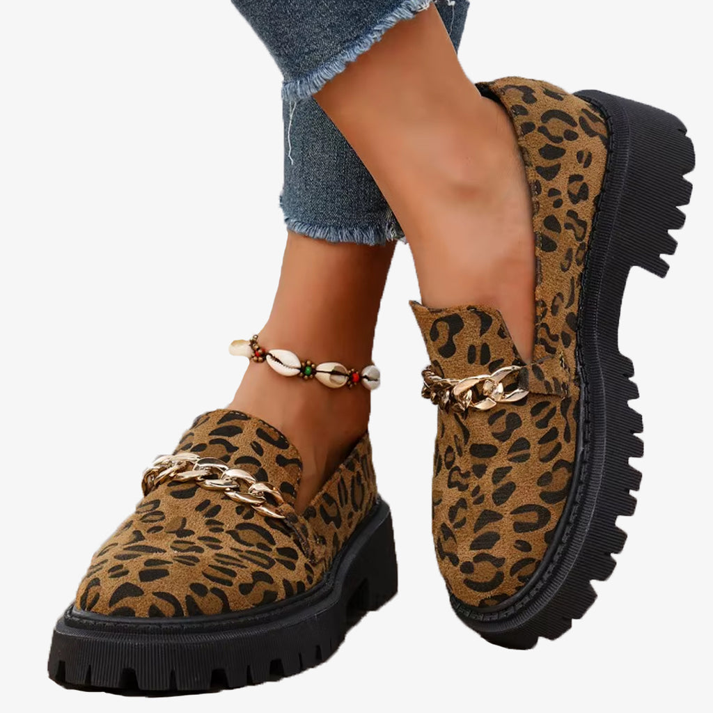 Coppia di mocassini leopardati in pelle scamosciata con plateau e catena, indossati con jeans e cavigliera conchiglia