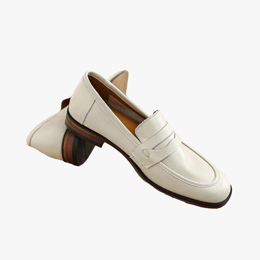 Si vede un paio di mocassini beige con suola marrone in vera pelle appoggiato su un tronchetto di legno