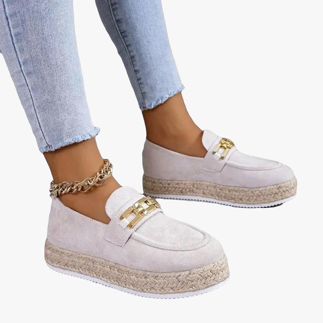 Si vedono i piedi di una donna in jeans che indossa mocassini con zeppa in camoscio sintetico di colore beige
