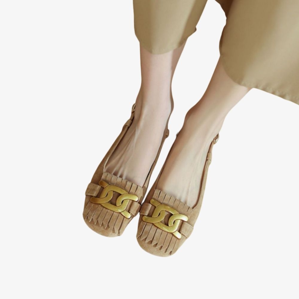 Mocassini beige con frange e una decorazione dorata sul collo del piede, indossati da una donna