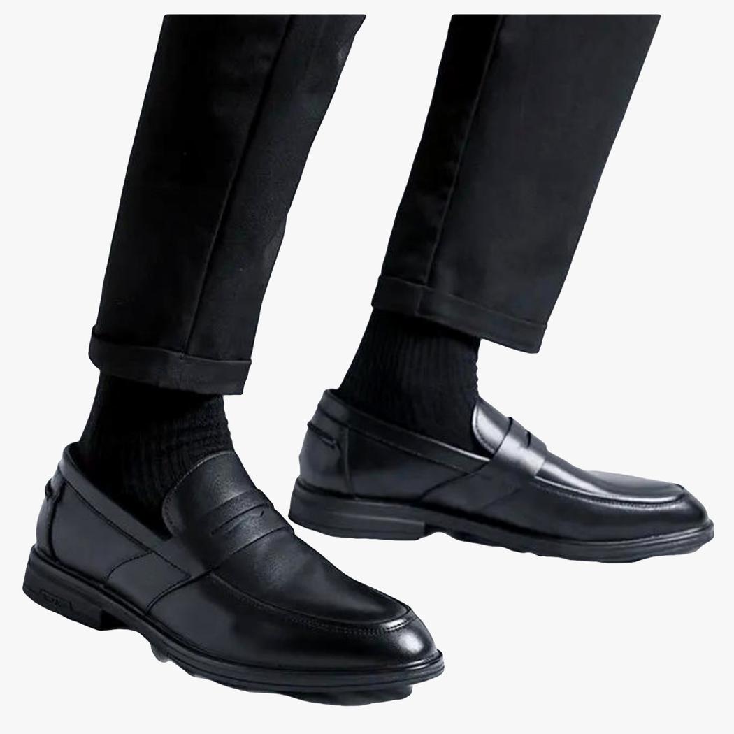 si vede su uno sfondo chiaro la parte bassa delle gambe di un uomo che indossa un pantalone nero e mocassini neri classici in pelle sintetica da uomo