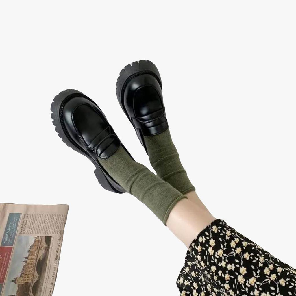 si vedono i piedi di una donna a terra, indossa calze kaki e mocassini neri con tacco quadrato e suola spessa