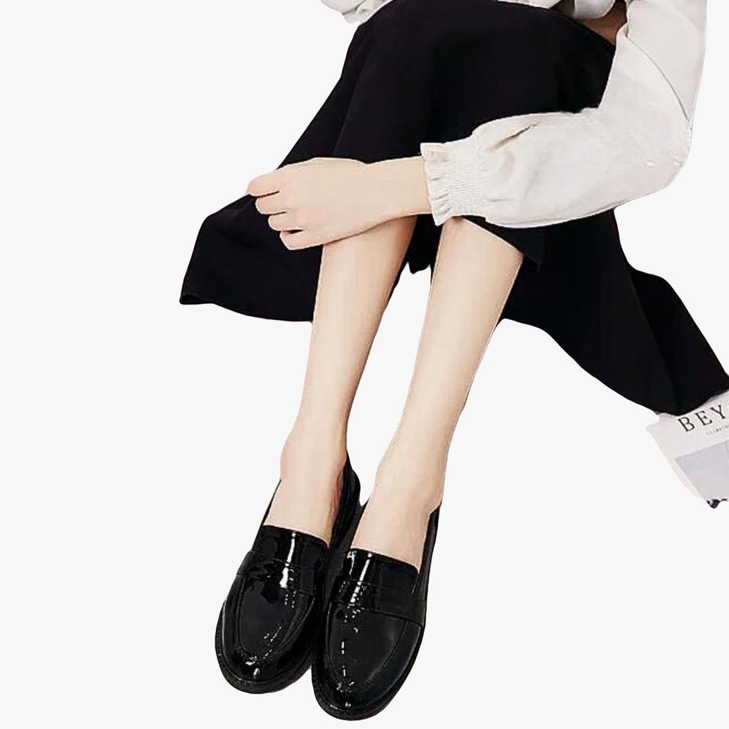 Si vede una donna seduta a terra, senza la parte superiore del corpo, che indossa un paio di mocassini neri con tacco quadrato in stile preppy