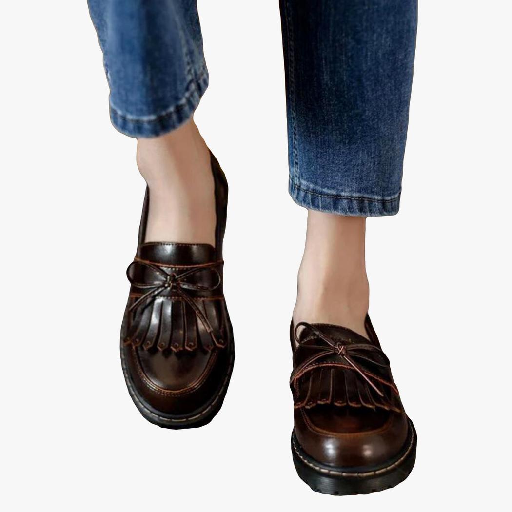 si vedono i piedi di una donna in jeans che indossa mocassini marroni con tacco quadrato e frange in stile vintage