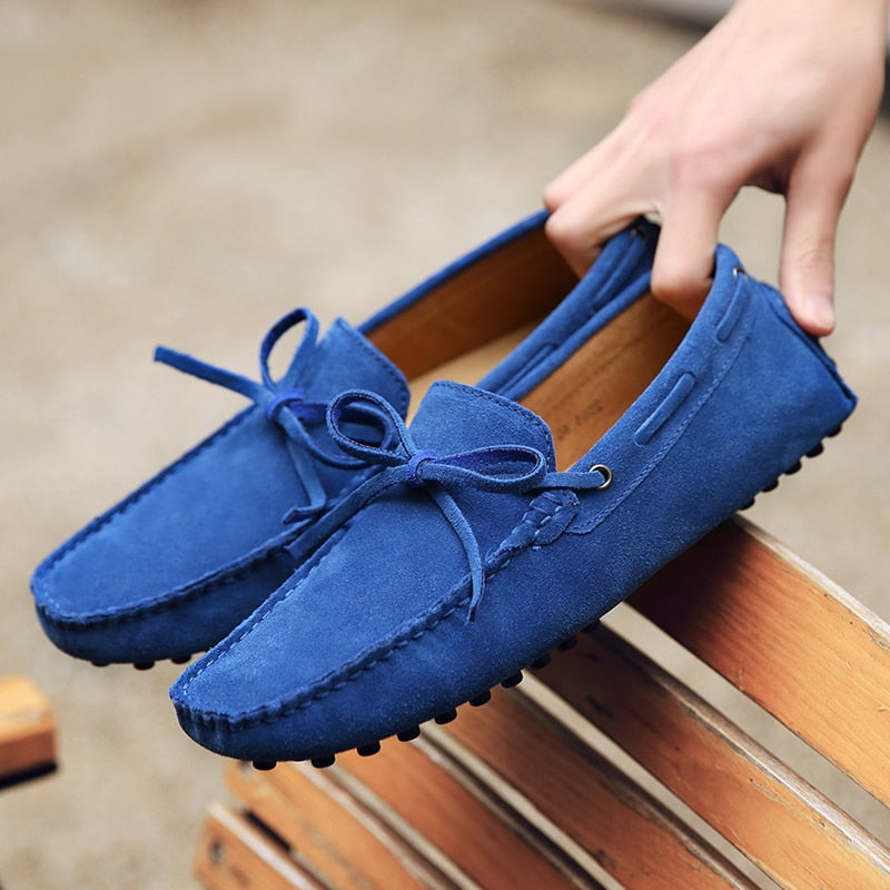 Coppia di mocassini blu tenuti in una mano su una panchina di legno