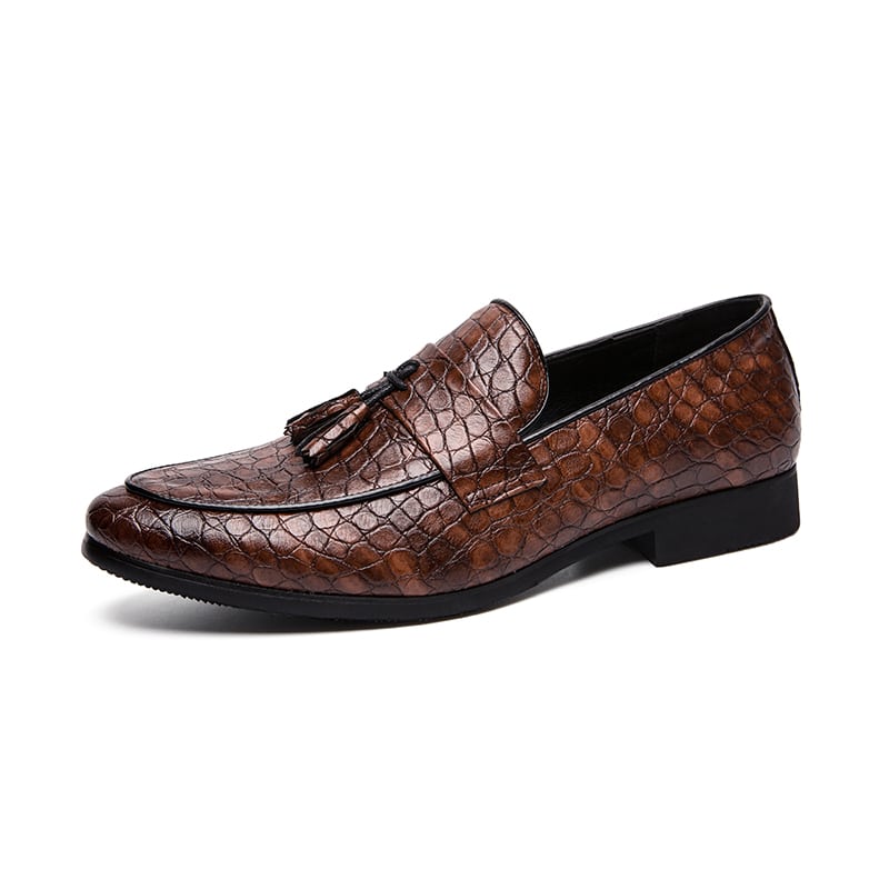 Un mocassino marrone in pelle di serpente con una fascia sulla parte superiore e nappe decorative, su sfondo bianco.
