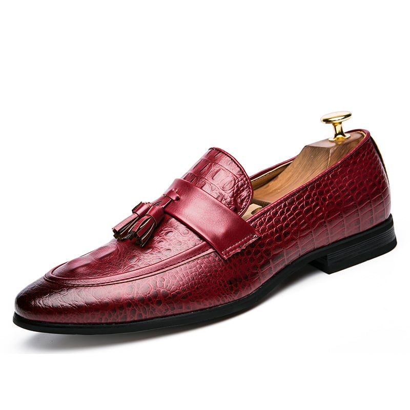 Un mocassino in pelle di coccodrillo rossa con nappina decorativa e punta scura su sfondo bianco.