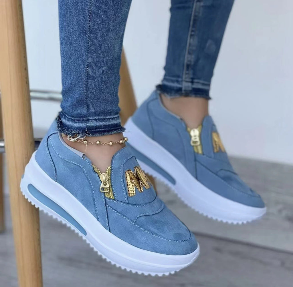 Mocassini blu con chiusura dorata, indossati da una persona di cui si vedono solo le caviglie.