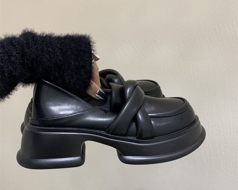 Mocassini con plateau neri da donna in pelle sintetica con sfondo beige e una donna che tiene in mano il paio di scarpe