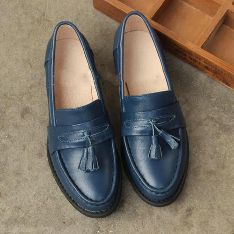 mocassino con tacco in pelle blu con nappina sulla parte superiore, su fondo grigio