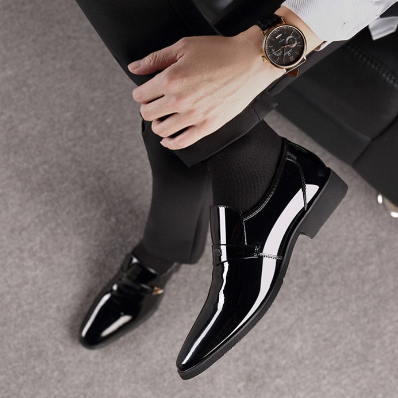 Piedi in mocassini di vernice nera. Gamba incrociata con orologio al polso.