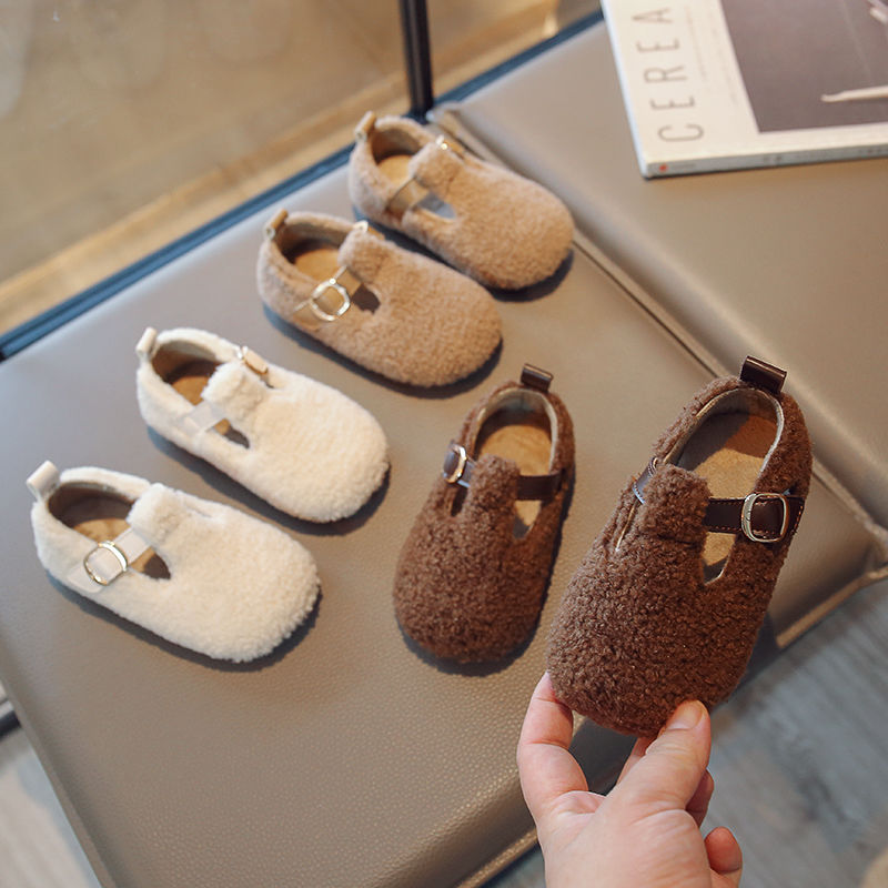 mocassino in pelliccia sintetica bianca, beige e marrone su un tavolo, un paio di mocassini in pelliccia marrone tenuti in una mano