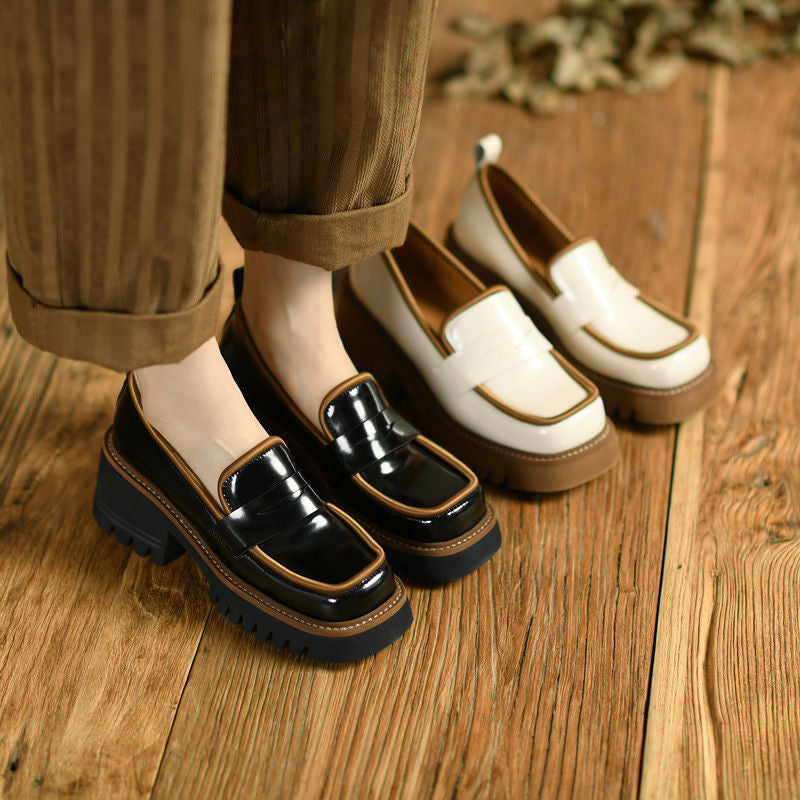 Due paia di mocassini in vernice a contrasto, uno beige e marrone, l'altro nero e marrone, ai piedi di una donna in piedi su un parquet che indossa pantaloni larghi a righe marroni.