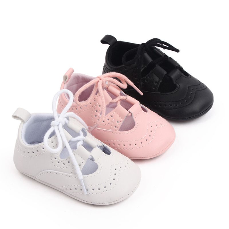 Tre mocassini stringati da bambino allineati in diagonale nei colori bianco, rosa e nero