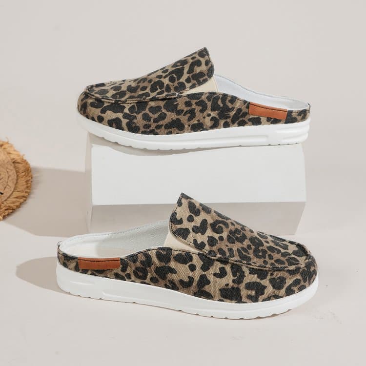 Mostrato di profilo, un paio di mocassini sportivi rotondi in tela con stampa leopardata e suola spessa bianca. Una scarpa su un espositore bianco e una sotto su un pavimento bianco