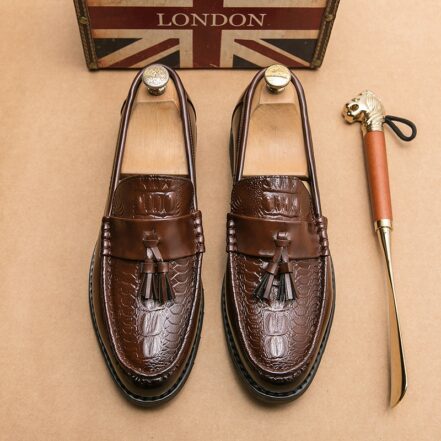 Mocassini con nappe marroni su pavimenti beige con accanto una scarpa color oro