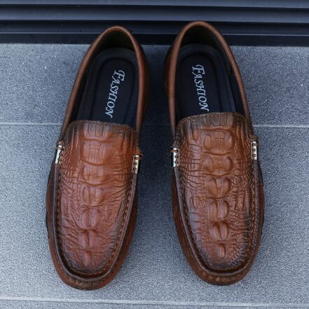 Mocassini in coccodrillo marrone su sfondo grigio.