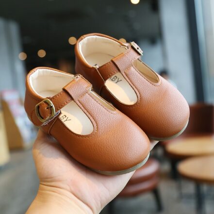 piccolo mocassino per bambine in ecopelle marrone indossato da una mano adulta