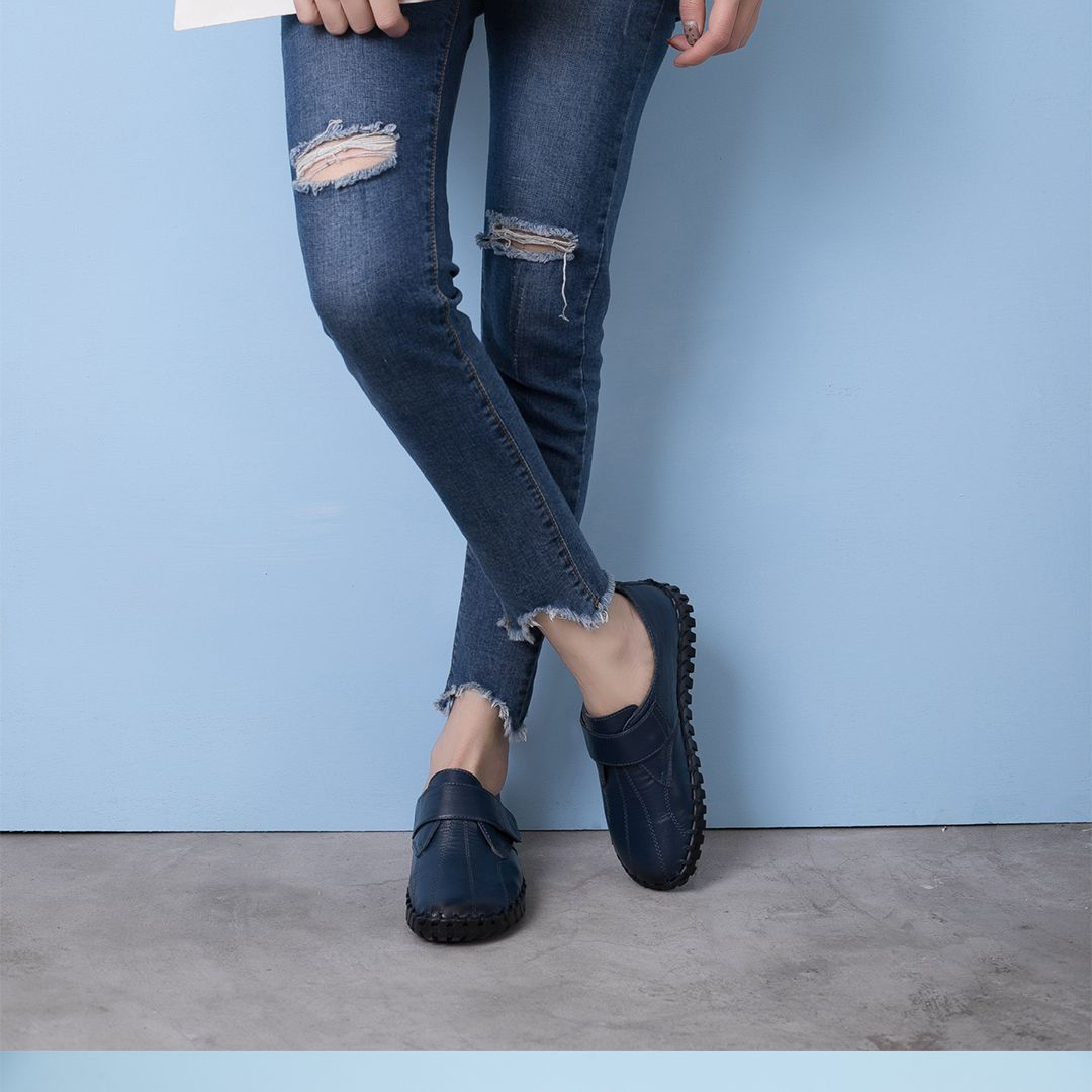 Gambe di una persona in piedi a gambe incrociate che indossa jeans bucati e scarpe blu.