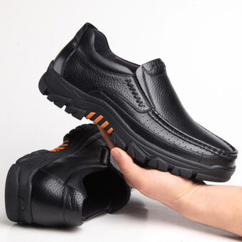 Fotografia di un paio di mocassini ortopedici in pelle nera con suola spessa. Una scarpa è appoggiata sul pavimento, l'altra è tenuta in una mano.