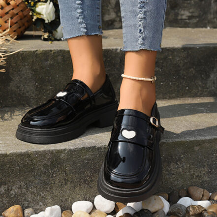 mocassini in vernice nera, con un cuore bianco sul davanti, indossati da una persona in jeans, in piedi sulle scale