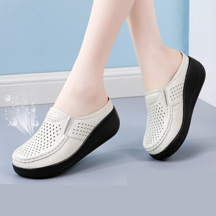 Una donna con le gambe incrociate che indossa mocassini bianchi con suole nere e robuste su un pavimento grigio