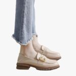 on voit les pieds d'une femme qui porte un jean, elle porte des mocassins beiges souples en cuir synthétique