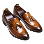 A pair of genuine leather tassel loafers for men can be seen on a brown background.