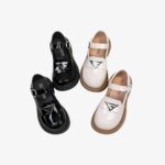 2 paires de mocassins brillants noirs et blancs avec détails argentés, sur fond gris.