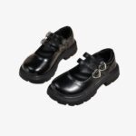 Paire de mocassins noirs avec double bride et un détail coeur dessus, sur fond gris.