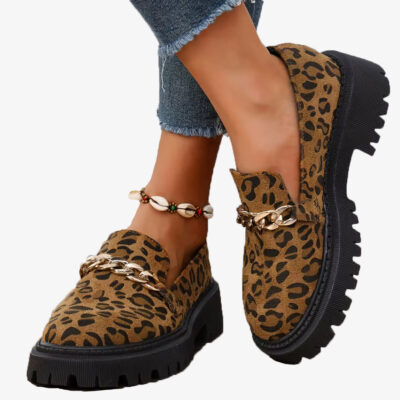 Coppia di mocassini leopardati in pelle scamosciata con plateau e catena, indossati con jeans e cavigliera conchiglia